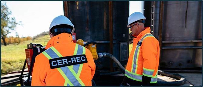 Deux membres du personnel de la Régie portant une veste de haute visibilité orange vif et un casque de protection blanc sont debout à l’extérieur, près d’une machine industrielle. 