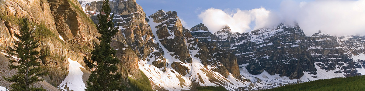 Panoramic view of the snow-capped Rocky Mountains with green grass in the foreground.