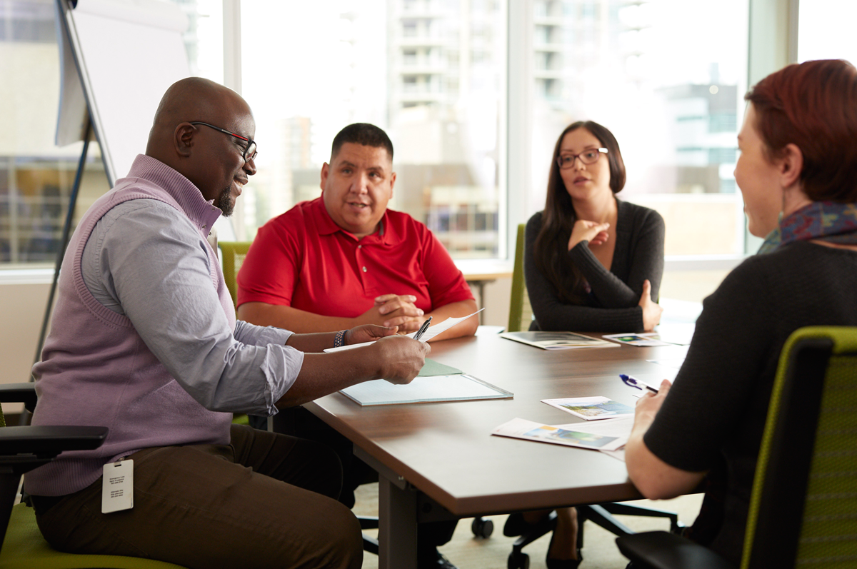 Two CER employees sitting for an informal meeting with two Indigenous individuals. They are discussing various printed information sheets.