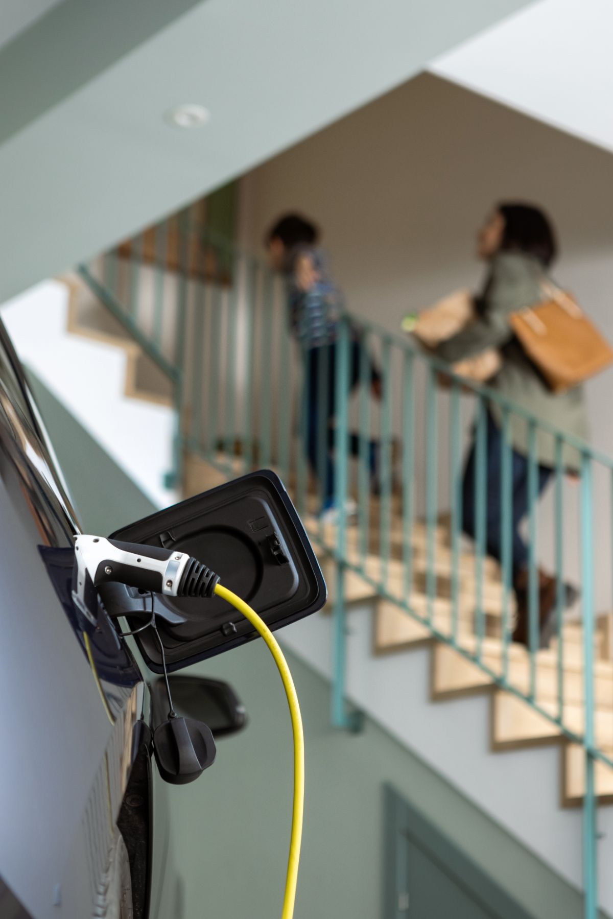 Mother and son walk into home while electric car charges in garage.