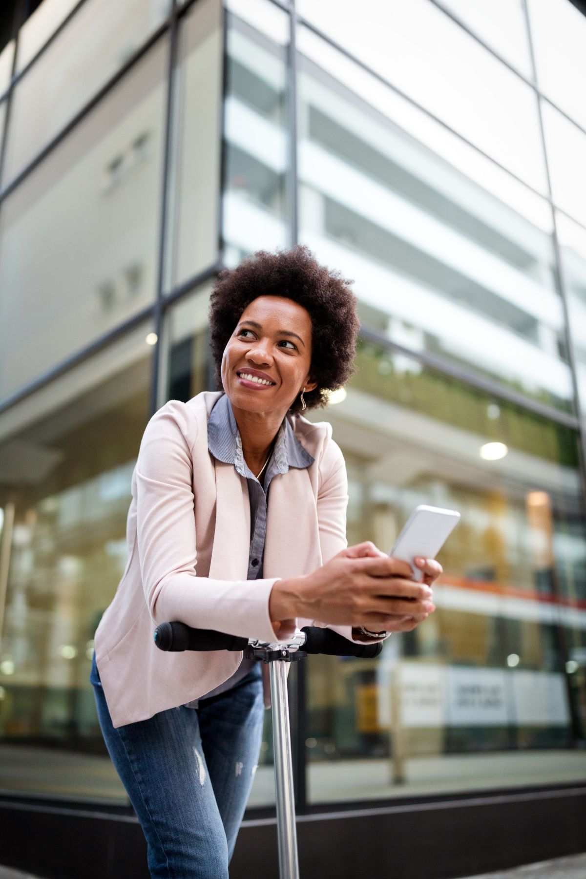 Smiling woman leans over electric scooter with smartphone in hand.