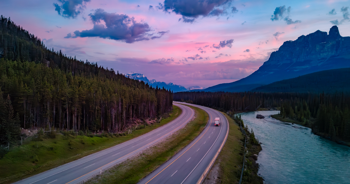 Un camion de transport sort du cadre sur la route transcanadienne, dans les Rocheuses canadiennes, alors que le soleil se lève.