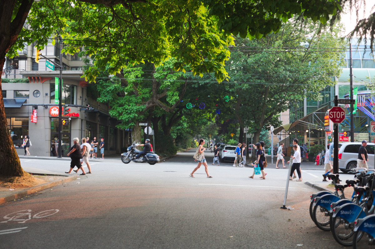 Une soirée d’été dans le centre-ville de Vancouver, une rue animée, des piétons qui traversent et des vélos de location stationnés près d'un coin.