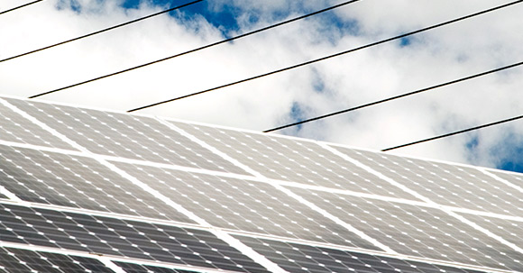 Solar panel detail with power lines against a cloudy sky.