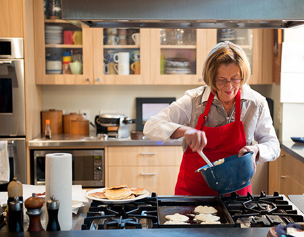 A woman in a red apron cooks pancakes on a natural gas range stove.