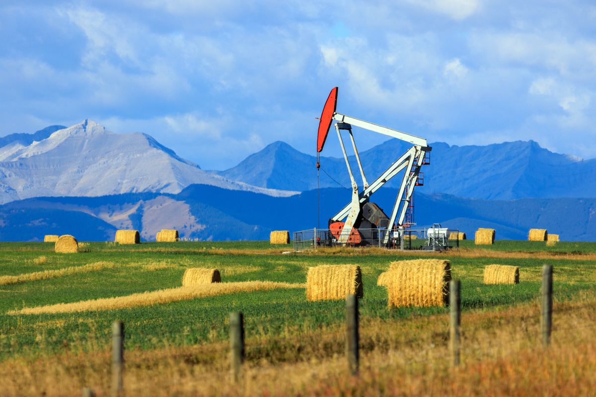 Tour de forage pétrolier dans un champ albertain avec montagnes en arrière-plan.