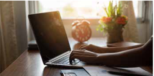 Someone works on a laptop as the sun shines through a window in the background.