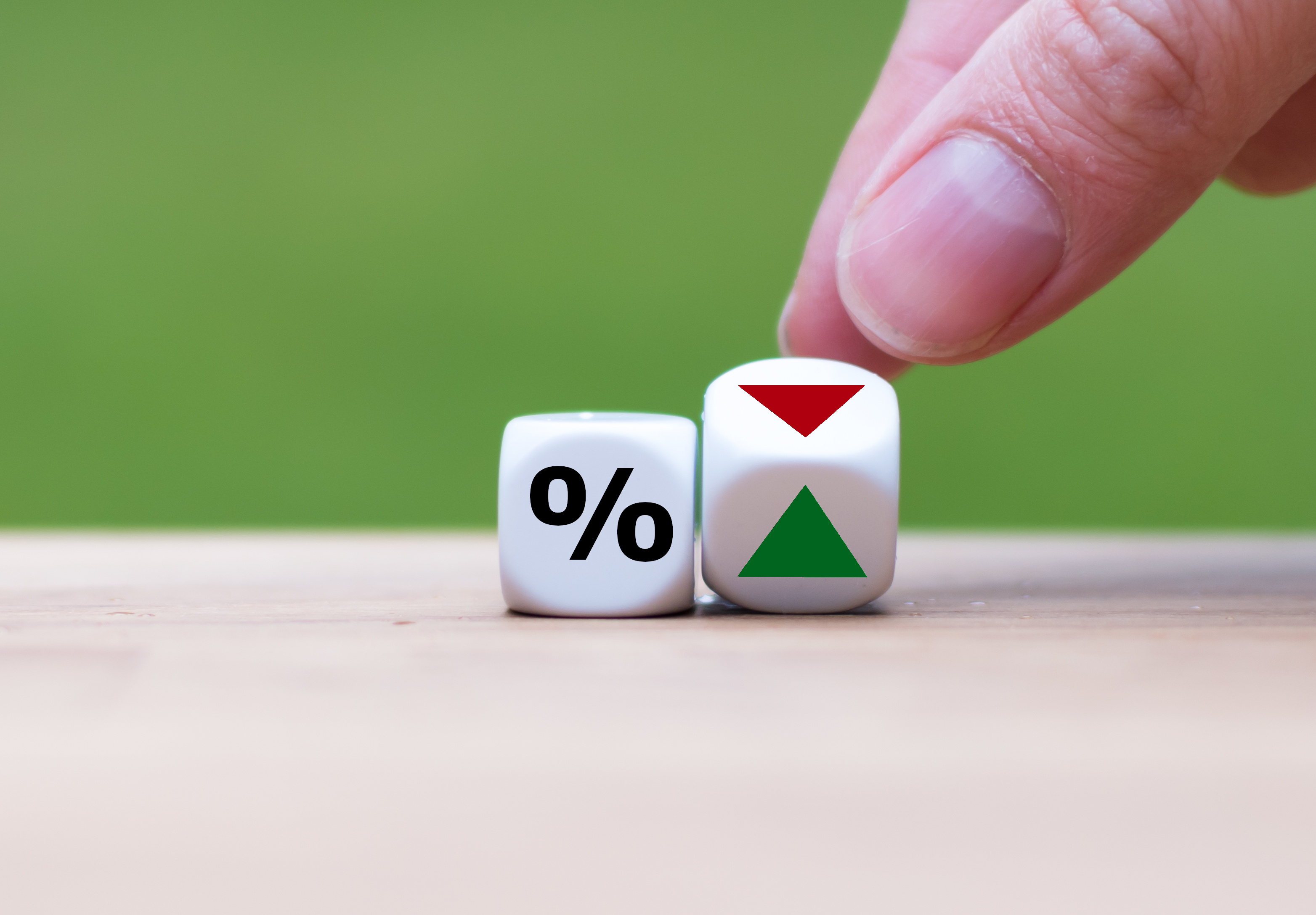 Une main déplace deux dés, l’un affichant un signe de pourcentage et l’autre, un triangle vert et un triangle rouge.